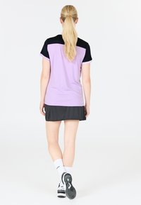 Kortærmet top i lys lilla med sorte detaljer på skuldrene, parret med en sort nederdel. Stoffet ser glat ud; sporty design.