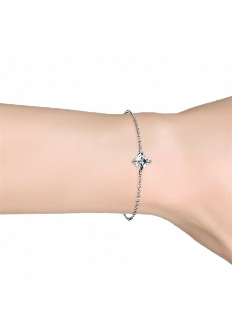 Bracciale in argento con un gemma trasparente a forma di diamante come pezzo centrale, mostrato su un polso contro uno sfondo semplice.