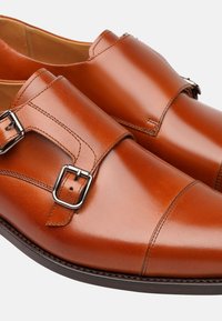 Scarpe marroni in pelle con doppio strap monaco, dal design elegante, texture liscia e fibbie in tonalità argento. Cuciture dettagliate sulla tomaia.