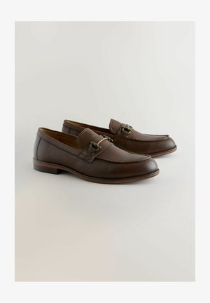 Mocassins en cuir marron à talon plat, avec une boucle décorative et des détails de couture, texture lisse et design à bout arrondi.