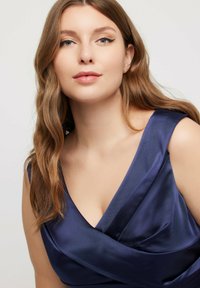 Satin marinblå klänning med djup halsringning och breda axelband, med en omsluten bodice-design och slät textur.