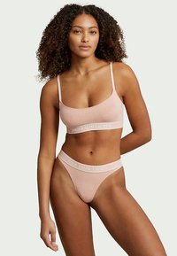 Lys rosa undertøysett bestående av en myk bralette med tynne stropper og matchende tanga, begge med subtil logo-detaljering.