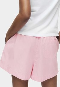 Shorts roses en tissu léger avec des fines rayures verticales, dotés de poches latérales et d'une poche arrière unique. Taille élastique.