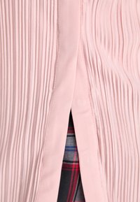Pink, pleated fabric with a subtle sheen, featuring a side opening revealing a blue, red, and gray plaid lining. Smooth texture.