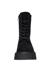 Botín de ante negro con puntera redonda, que presenta cordones en la parte delantera, una cremallera lateral y una suela de goma negra gruesa. Superficie texturizada visible.