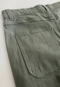Olive green cotton pants with a flat back pocket, subtle texture, and stitched waistband details, viewed from an angled overhead perspective.
