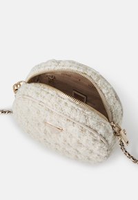 Borsa rotonda in tessuto cream texturizzato con accenti in filo dorato, dotata di una cerniera dorata, di una tracolla a catena e di una fodera interna beige.
