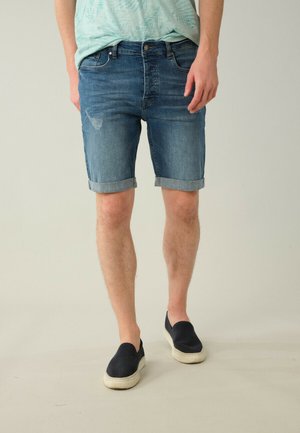 Shorts en jean bleu foncé, avec un design classique à cinq poches, des ourlets repliés et une légère décoloration sur le devant. Associés à des chaussures slip-on bleu marine.