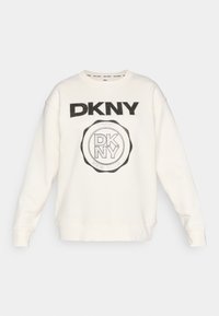 Felpa bianca con logo DKNY nero in testo bold e design circolare. Presenta polsini e orlo a costine con un tessuto morbido e texturizzato.