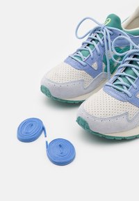 Ljusblå och teal mocka och mesh sneakers med perforerade vita läderaccenter, tillsammans med två rullar blå skosnören.