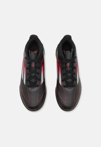 Czarne buty sportowe z czerwonymi akcentami i białymi paskami, z teksturowanym cholewką, sznurowaniem i gładką gumową podeszwą.