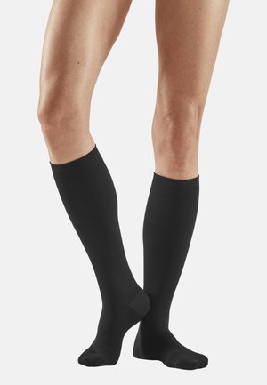 Schwarze knielange Socken mit einem strukturierten Muster und dehnbarem Stoff. Sie verfügen über eine verstärkte Zehenpartie und einen glatten, gerippten Bund oben.