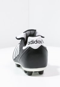 Crampons de soccer noirs en cuir avec des accents blancs, dotés d'un col rembourré, d'un design à trois bandes et d'une semelle extérieure à crampons noirs.