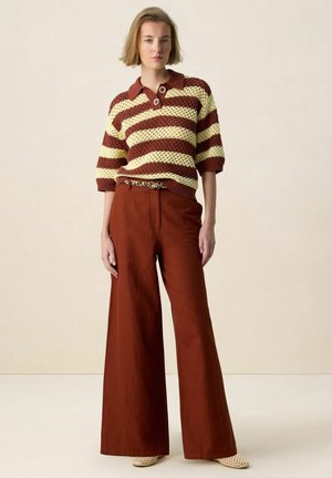 Woman wearing a brown and cream striped knit top with wide-leg rust-colored pants and leopard print belt, standing against a neutral background.