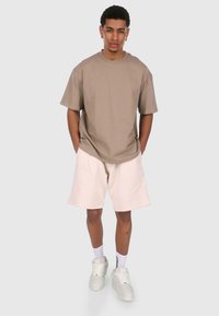 Beige bomulds t-shirt med korte ærmer, parret med lyse beige shorts. Hvide sneakers og sokker fuldender det afslappede outfit.