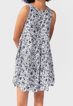 Robe à imprimé floral avec une conception sans manches, un col rond, un ourlet à volants, et un fond blanc avec des fleurs bleues. Texture de tissu douce.
