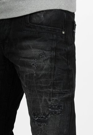 Schwarze Jeans aus Denim mit einem zerstörten Design und ausgefranstem Patch. Der Stoff hat eine leicht verblasste Textur und kontrastierende Nähte.