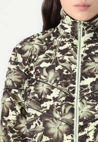 Floral-patterned jacket with high collar, featuring a dark brown and light green color scheme. Front zip closure and textured fabric detail.