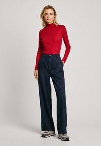Top de manga larga rojo acanalado combinado con pantalones de pierna ancha a rayas azul marino. Los pantalones cuentan con un cierre de botón y bolsillos laterales. Zapatillas cómodas.