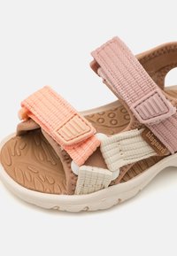 Lapsen avonaiset sandaalit, joissa on säädettävät vaaleanpunaiset ja persikanväriset hihnat, teksturoitu ruskea pohja ja valkoinen pohja valkoista taustaa vasten.