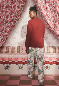 Czerwona koszula z długim rękawem zestawiona z wzorzystymi spodniami piżamowymi z kolorowymi ilustracjami na jasnym tle. Miękki materiał i luźny krój.