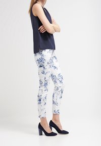 Mörkblå ärmlös topp i kombination med blommig mönstrad smalbyxa i vitt och blått, avslutad med mörkblå högklackade skor.