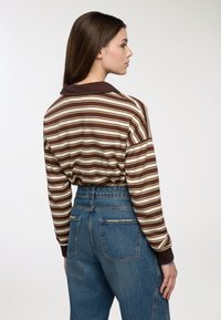 Camicia a maniche lunghe a righe marroni e crema con colletto marrone, abbinata a jeans in denim blu a vita alta con tasche posteriori.