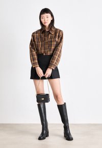 Braun- und schwarz-karierter, kurzes Hemd, schwarzer Minirock, schwarze kniehohe Stiefel und eine kleine schwarze Tasche mit einer goldenen Kettenriemen.