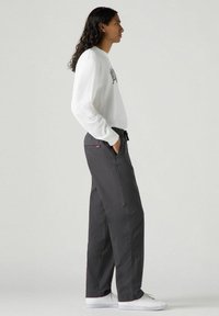 Pantaloni di cotone grigi con una vestibilità comoda, dotati di una vita elasticizzata e tasche laterali. Abbinati a una camicia bianca a maniche lunghe.