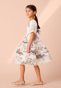 Obleka s cvetličnim vzorcem v beli barvi s vijoličnimi in zelenimi cvetovi, kratkimi napihnjenimi rokavi ter pentljo na hrbtni strani. Nošena z zlatimi metalik balerinkami.