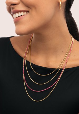 Collares en capas dorados y rosas con cadenas suaves y pequeñas cuentas, llevados sobre una camiseta negra, resaltando el diseño elegante y la textura.