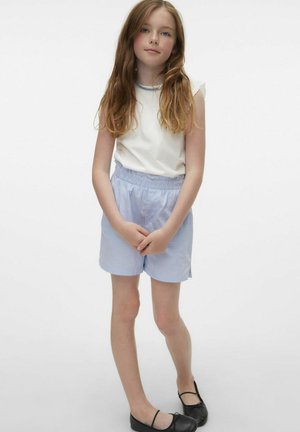 Haut sans manches blanc avec bordure en dentelle, associé à un short rayé léger bleu et blanc. Des chaussures plates noires complètent la tenue.