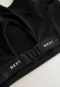 Crni sportski grudnjak s mrežastim panelima, elastičnom trakom ispod grudi s "NEXT" brendiranjem i zatvaranjem na kuka i oko za prilagodljivo pristajanje.