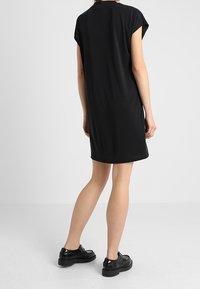 Schwarzes kurzes Kleid mit kurzen Ärmeln aus weichem Stoff, mit lockerer Passform, einem runden Halsausschnitt und einer leichten A-Linien-Silhouette. Tragen mit schwarzen Schuhen.