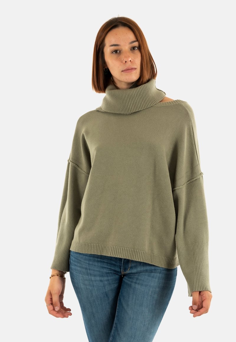 Maglione verde oversize con un alto collo a costine, cuciture delle spalle a caduta e lavorazione a maglia testurizzata. Abbinato a jeans in denim blu.