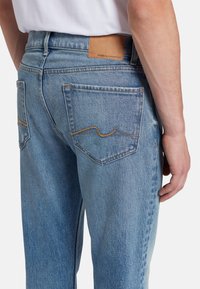 Jeans in denim blu chiaro con una vestibilità slim, dotati di una patch in pelle sulla vita, cuciture distintive sulle tasche posteriori e una texture sbiadita.