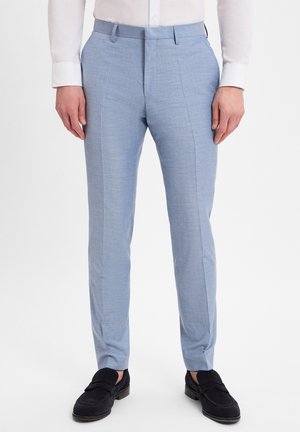 Hellblaue maßgeschneiderte Hosen aus strukturiertem Stoff, mit einer glatten Oberfläche und schmal zulaufendem Bein. Kombiniert mit dunklen Schuhen.