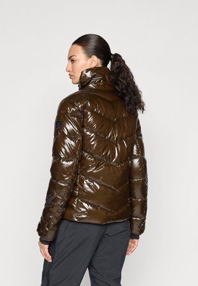 Barna fényes puff-jacket, chevron varrással, magas gallérral és cipzáras zsebekkel. A tenyéren egy logó matricát tartalmaz.