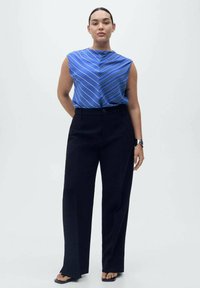 Blue sleeveless top with white diagonal stripes, paired with high-waisted black trousers. Smooth fabric with a loose fit, minimalist design.