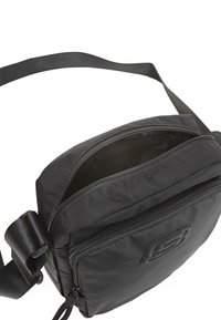 Bolso cruzado negro hecho de un tejido duradero, con un compartimento principal con cremallera y un bolsillo frontal con cremallera. Incluye una correa ajustable.