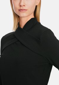 Schwarzes Strickoberteil mit einem einzigartigen Wickeldesign am Kragen und einer glatten Textur, das eine taillierte Silhouette hervorhebt.