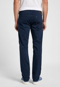 Pantaloni slim-fit blu navy realizzati in tessuto morbido, con due tasche posteriori dotate di cuciture curve e una patch-logo vicino alla vita.