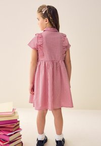 Rot-weißer Gingham-Kinderkleid mit plissierten Ärmeln, einem Kragen und geraffter Taille; kombiniert mit schwarzen Schuhen und weißen Knöchelsocken.