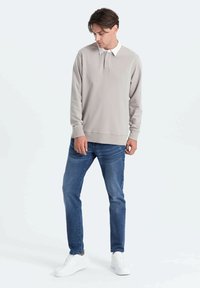 Polo grigio chiaro a maniche lunghe con colletto bianco, abbinato a jeans blu e sneakers bianche. Design semplice e aderente, texture liscia.