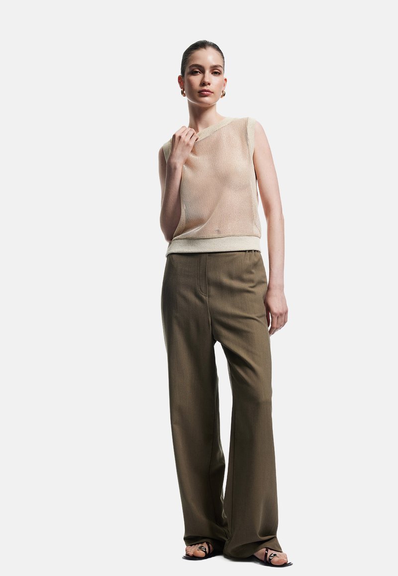 Strikket ærmeløs top i lys beige kombineret med olivengrønne vide bukser og sorte sandaler med dekorative stropper.