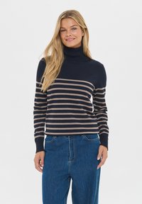 Sweter w paski w kolorze granatowym i beżowym z wysokim kołnierzem oraz ściągaczami, zestawiony z luźnymi niebieskimi dżinsami. Gładka tekstura, casualowy fason.