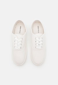 Vita canvas sneakers med rund tå, fem hål för snörning och vita snören. Har en slät textur och en enkel design. Märkt "ANNA FIELD."