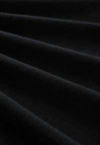 Czarna tkanina o gładkiej fakturze, ukazana w fałdach, podkreślająca miękkość i głębokość koloru. Brak widocznych wzorów lub elementów metalowych.