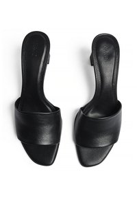 Sandales ouvertes en cuir noir avec une large sangle sur le dessus et un bout carré. Texture lisse, talon plat, design minimaliste.