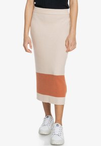 Jupe mi-longue côtelée beige avec une bande horizontale orange et blanche. Texture douce, coupe ajustée, portée avec des baskets blanches.